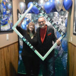 Two people posing at a festive photo booth with blue balloons.
