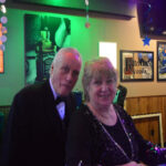 An elderly couple dressed formally at a party with green lighting.