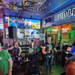 A lively bar scene with musicians performing live in front of colorful lights.