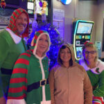 Four people in festive Christmas sweaters and pajamas posing indoors.